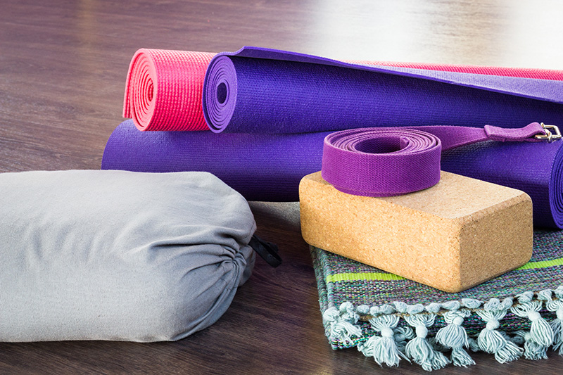 Variety of yoga props on wooden floor in studio. Pink and purple Restorative/Yin Yoga